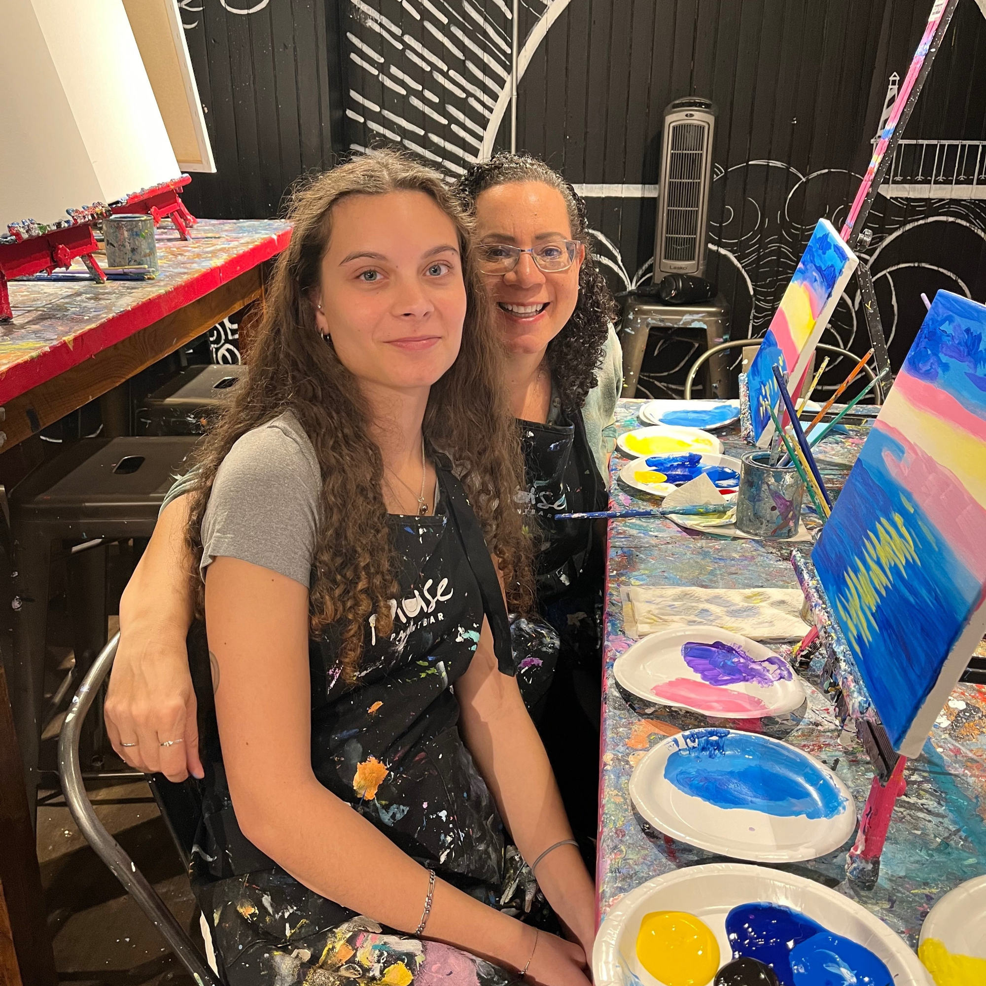 A mother and daughter sitting in front of easels and paint at a paint & sip event.