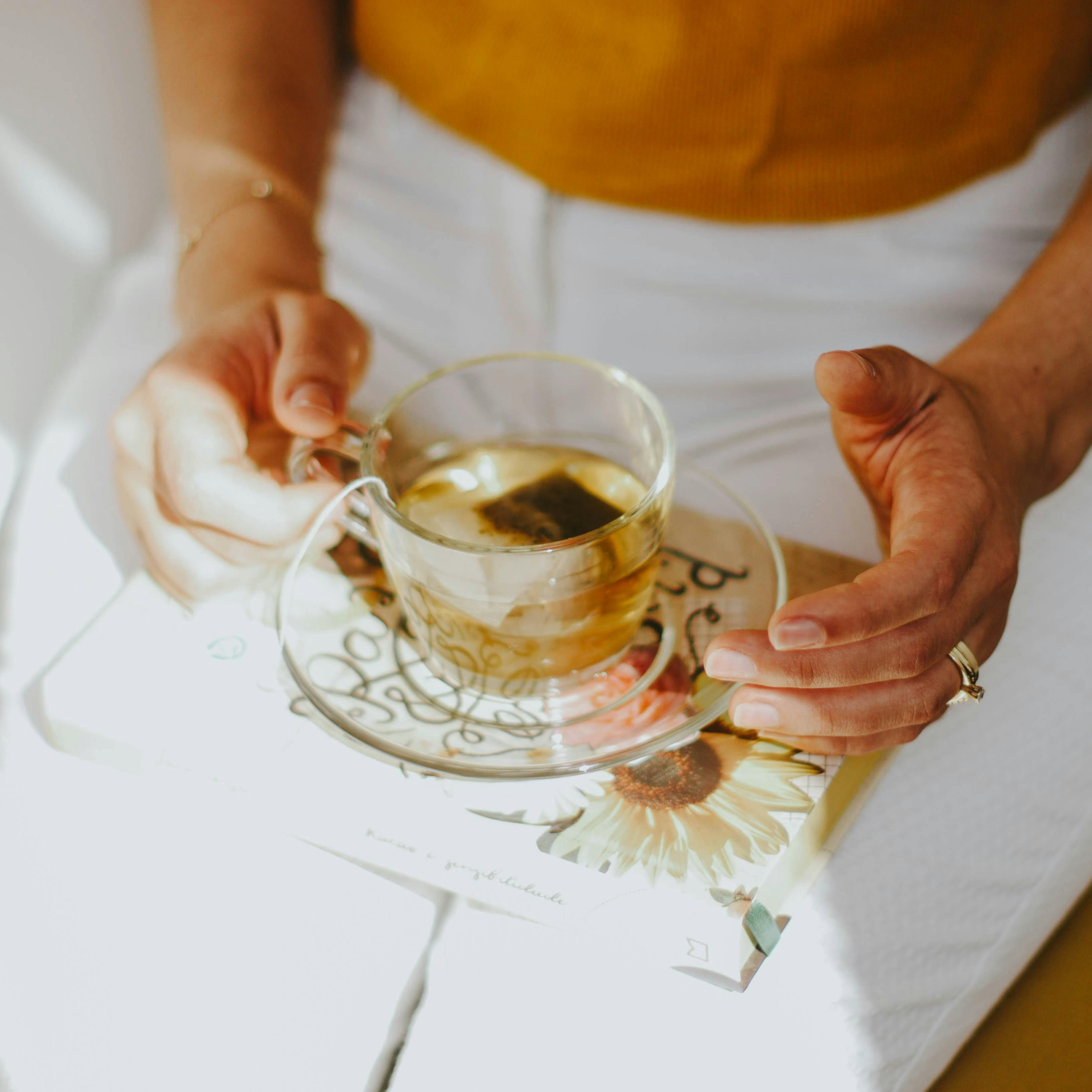 Close up photo of woman balancing a book and cup of tea on her lap